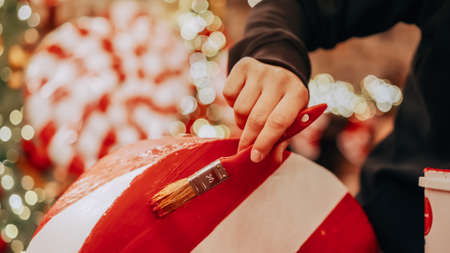 Close up of female hands with brush, girl paints Christmas or New Year decoration in white and red. The concept of preparation for Christmas and New Yearの写真素材