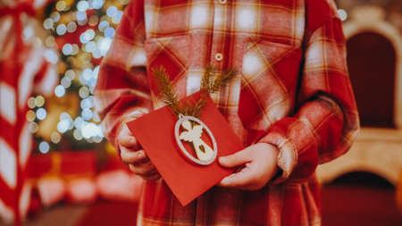 Unrecognizable child holding a decorated letter for Santa Claus. Decorated Christmas letter in the hands of a little boy. Christmas celebration concept.の写真素材