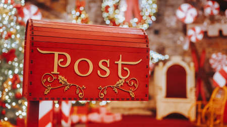 Closeup Red post box for letters to Lapland to Santa Claus. Christmas tradition. Decorative mailbox Santa Claus workshop, wrapped gifts presents boxes on holiday eve in night on xmas backgroundの写真素材