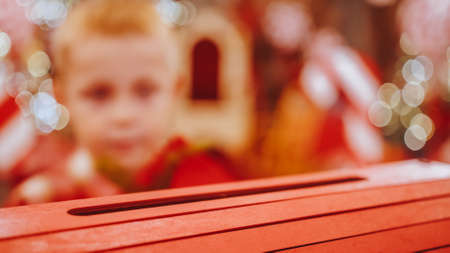 An unrecognizable boy sends a letter to Santa Claus. Close up of a red Christmas letter being thrown in a mailbox. The child sends a letter to Santa Claus.の写真素材