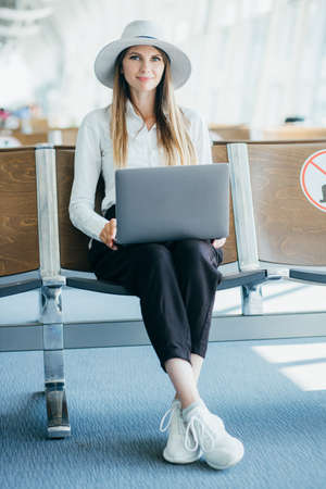Young elegant business woman with hand luggage in international airport terminal, working on her laptop while waiting for flight.の写真素材