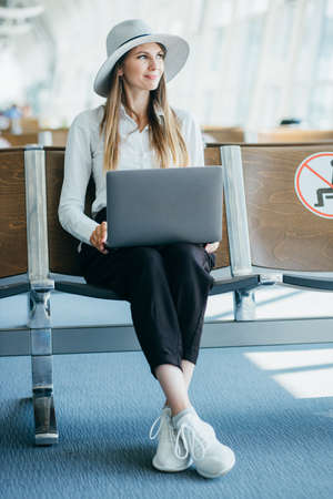 Young elegant business woman with hand luggage in international airport terminal, working on her laptop while waiting for flight.の写真素材