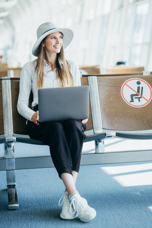 Woman waiting his flight at airport terminal, sitting on chair and typing on the laptop looking side. Top viewの写真素材