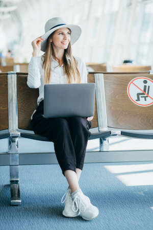 Woman waiting his flight at airport terminal, sitting on chair and typing on the laptop looking side. Top viewの写真素材