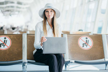 She always travels with tablet. Beautiful girl enjoying her laptop while sitting in airport lounge hall, looking at camera and smiling.の写真素材