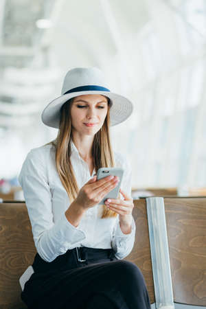 Casual young woman using her cell phone while waiting to board a plane at the departure gateの写真素材