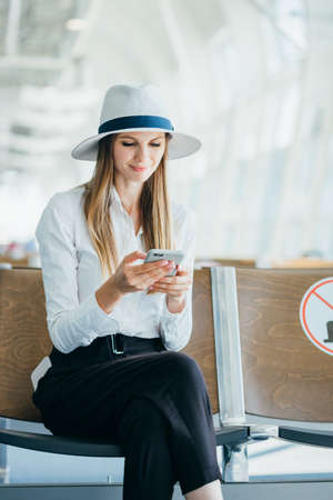 Casual young woman using her cell phone while waiting to board a plane at the departure gateの写真素材