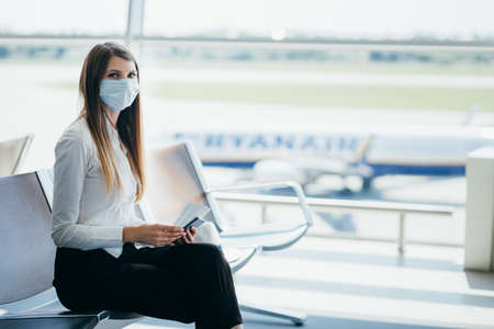Beautiful business woman at the airport, using the phone to send text messages, standing by the window in the corporate office building, checking messages. The girl is holding tickets and a passport.の写真素材