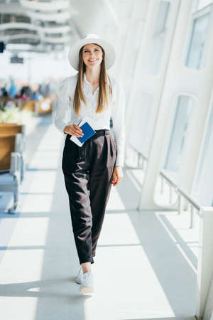 Cheerful businesswoman waiting for her flight at airport. Young woman at the airport. Pretty young female passenger at the airport shallow DOF color toned imageの写真素材