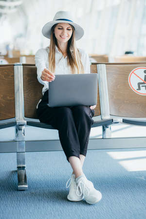 Young woman holding a laptop on lap typing keyboard indoors in airport.の写真素材