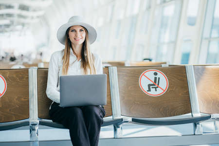 Airport or train station, Woman keep safe distance and working on laptop in airport terminal. Passenger prevent themselves from infection. Freelancer works and waits for flight in waiting room.の写真素材