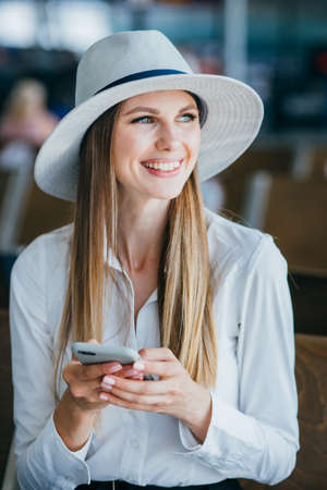 Airport business woman on smart phone at gate waiting in terminal. Air travel concept with young casual businesswoman sitting with hand luggage suitcase. Beautiful young mixed race female professionalの写真素材