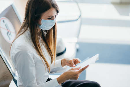 Female wearing protective mask is standing at the window in the airport terminal awaiting the departure of a flight due to travel restrictions due to the virus pandemic.の写真素材