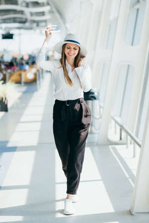 Cheerful businesswoman waiting for her flight at airport. Young woman at the airport. Woman is waiting her flight in waiting hall in airport. Happy young businesswoman looking at her air ticket.の写真素材