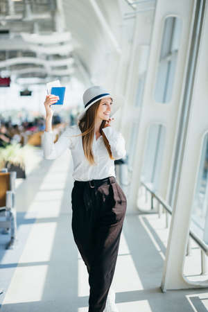 Cheerful businesswoman waiting for her flight at airport. Young woman at the airport. Woman is flight in waiting hall in airport. Smiling waiting her flight at airport terminal waiting roomの写真素材
