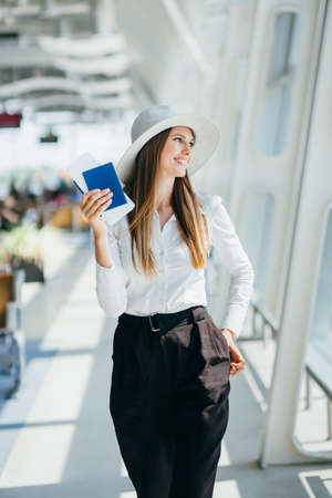 Cheerful businesswoman waiting for her flight at airport. Young woman at the airport. Woman is waiting flight in waiting hall in airport. Woman holding passport and boarding pass at airport.の写真素材