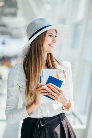 Elegant beautiful business girl holding travel tickets and using phone, happy girl looking at camera in airport terminal. Fashion woman portrait. Airport terminal. Business trip.の写真素材