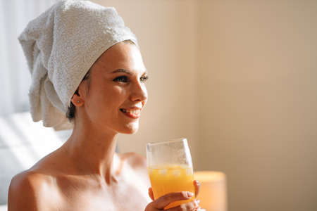 Lady wrapped in towel using laptop and drinking juice on bed.の写真素材