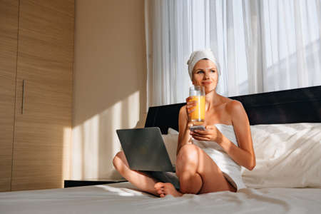 Woman in towel using mobile and laptop at hotel room.の写真素材