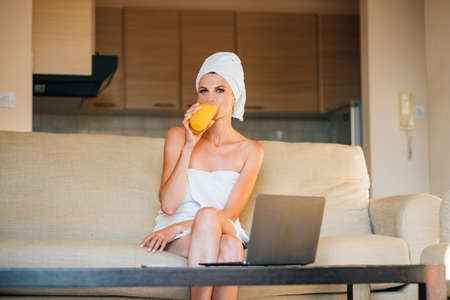 Healthy woman using laptop and drinking orange juice. adorable smiling happy working on laptop which standing on kitchen table and drinking orange juice in break between work,front view.の写真素材