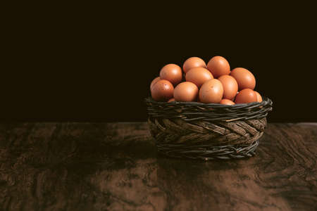 Bunch of eggs in a basket on a wooden old retro table with black backgroundの写真素材