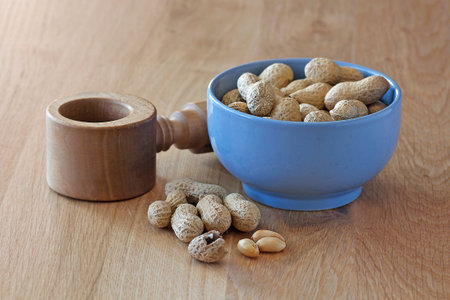 Nuts - peanuts in a bowl and wooden press on kitchen tableの写真素材