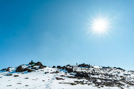 Horizontal shot from below the summit of snow-capped Province mountain with climbers and sun lens flare, Chileの写真素材