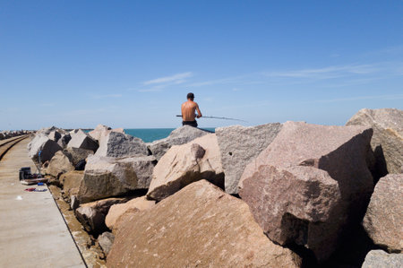 Fisherman on top of breakwater stones, waiting for the fish to catchの写真素材