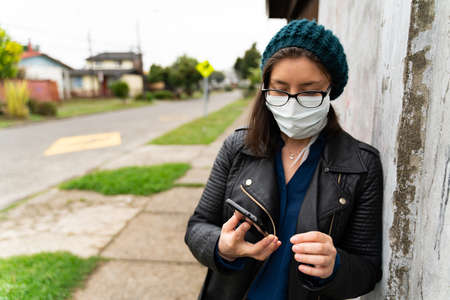 woman with mask looks at her cell phone on the streetの写真素材