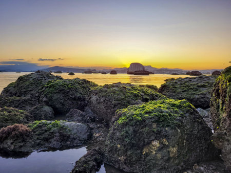 Photo of a beautiful, yellowish sunset, in a bay full of rocksの写真素材