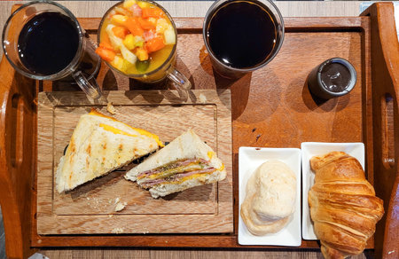 Photo of a breakfast, aerial view, containing black tea, coffee, fruit salad, bread and croissant