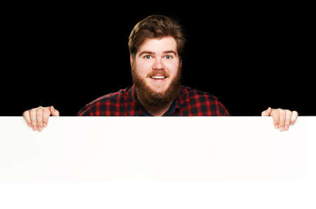 Happy guy smiles at the camera peeking behind wall on a black backgroundの写真素材