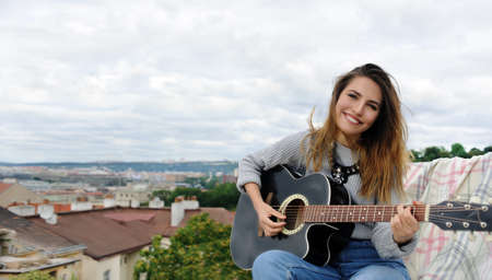 Girl playing the guitar on the background of the park on the roofの写真素材