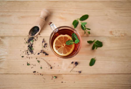 Top view on the glass cup of tea on the pile of dried tea herbs on the wooden backgroundの写真素材