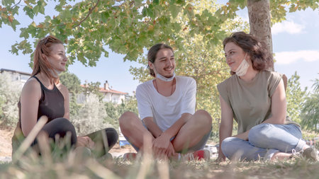 Young friends talking and laughing while sitting on grass. Meeting with friends in the park during...