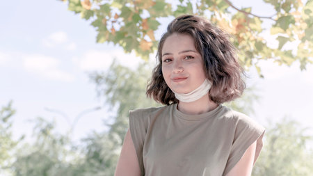 Portrait of young charming woman in medical mask. Her face mask is under the chin. New normality...