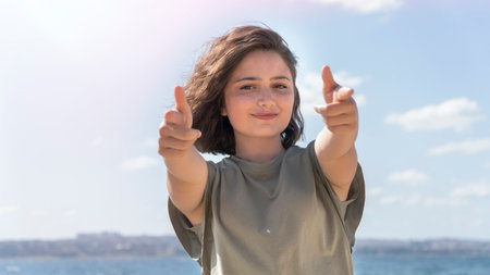 Young beautiful woman doing double thumbs up at the seaside. Gesturing that all is great. Outdoors shooting.の写真素材