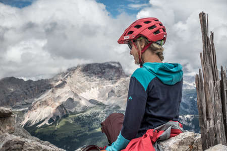 Young woman with blond hair, mtb helmet and sunglasses is sitting on a hiking trail in the Austrian Alpsのeditorial素材