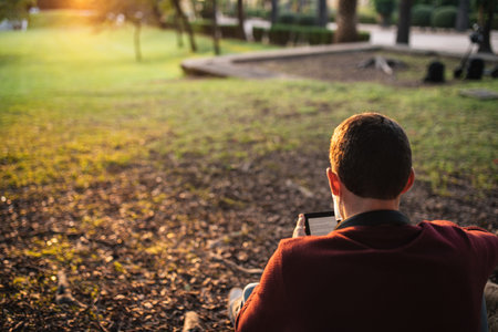 boy with a mask by the covid-19, reading an e-book, sitting in a tree at sunset.の写真素材