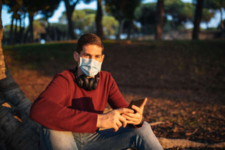 boy with a mask by the covid-19, reading an e-book, sitting in a tree at sunset.の写真素材