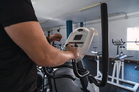 Unrecognizable man hands on elliptical trainer handrails in sport club. Cardio workout background, running on treadmill. Healthy lifestyle, guy training in gym.の写真素材