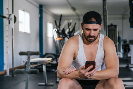 A man with a smart phone in the gym. Looking at the screen of the smart phone. health and wellness concept.の写真素材