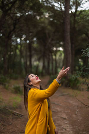 Beautiful woman throwing her hat in the air with a yellow coat in nature. Smile. Concept of freedom.の写真素材