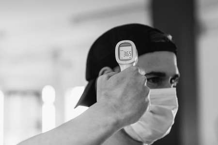 Man with mask taking his temperature. Infrared thermometer. Healthy gym. Pandemic . Concept of health and safetyの写真素材