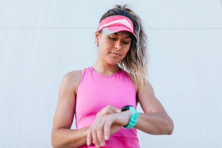 A young sports girl looks at a smart watch on her hand and checks her pulse, takes a break after jogging.の写真素材
