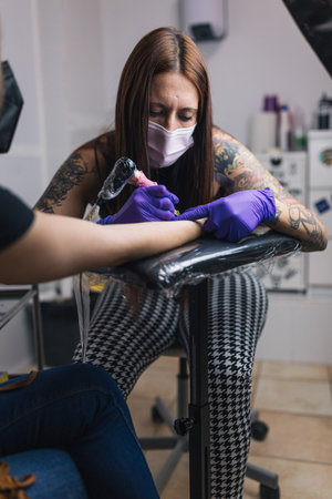 Tattoo artist tattooing in her studio with gloves and mask. Tattoo arm.の写真素材