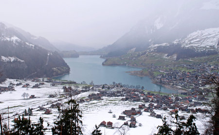 Swiss alpine lake and village in winter(Switzerland). Snowing, overcast sky and fog