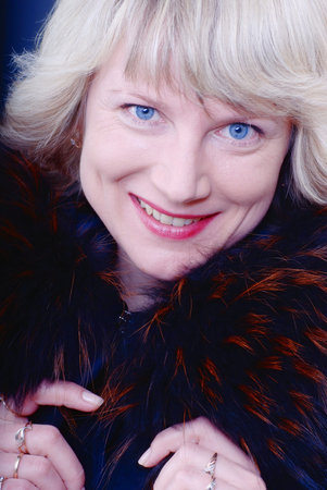 A portrait of adult beautiful smiling blond woman with blue eyes and red lips wearing a winter fur...