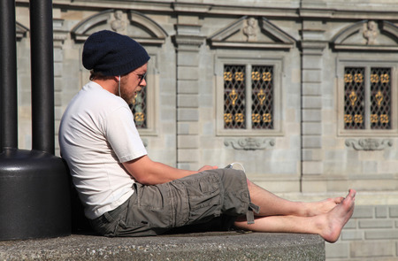 ZURICH, SWITZERLAND - MAY 05, 2013: Young barefoot man listen music in ipod headphone on embankment Limmat river, Zurich, Switzerlandのeditorial素材