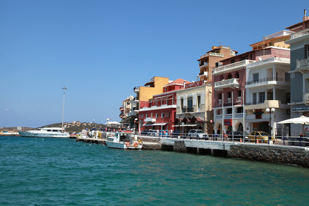 AGIOS NIKOLAOS, GREECE - JULY 18, 2012: Waterfront with outdoor greek tavern, small shops and boats in harbor of Agios Nikolaos, Crete, Greece.のeditorial素材